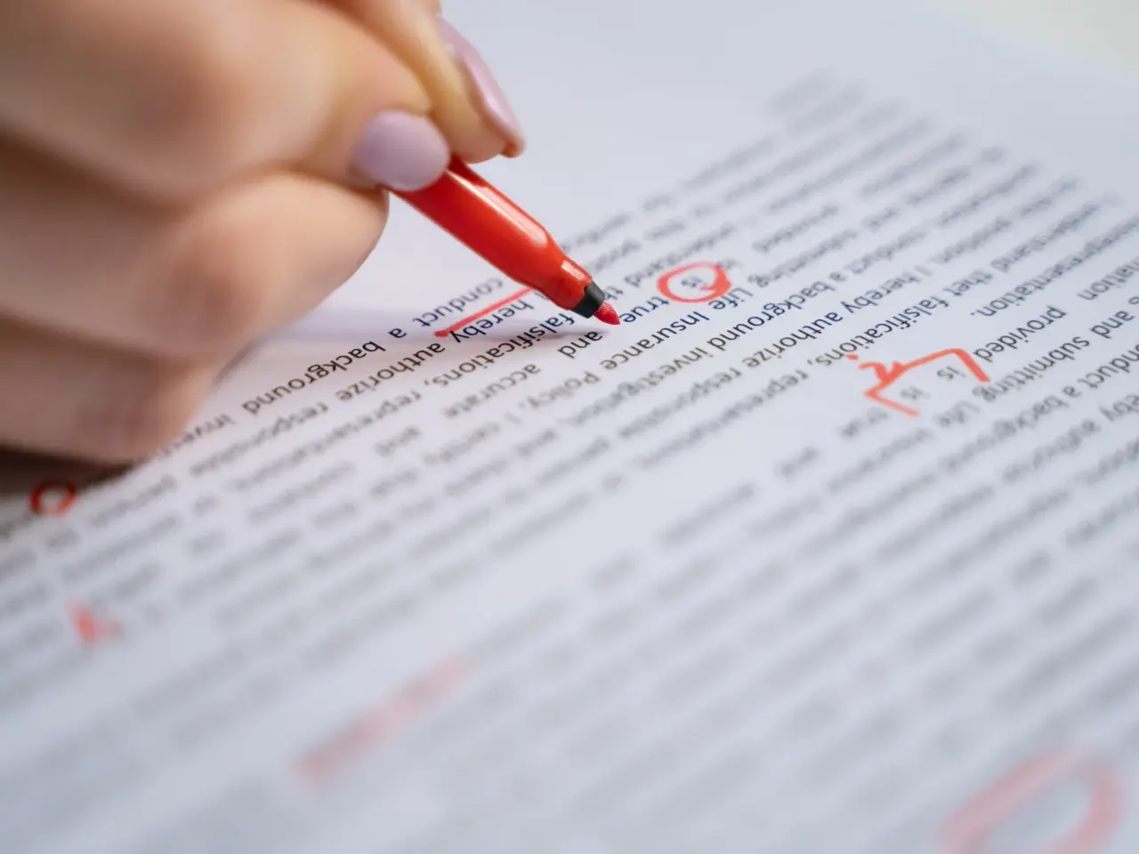 Close-up of a red pen marking corrections on a printed English document, symbolizing editing, proofreading, or document translation services.