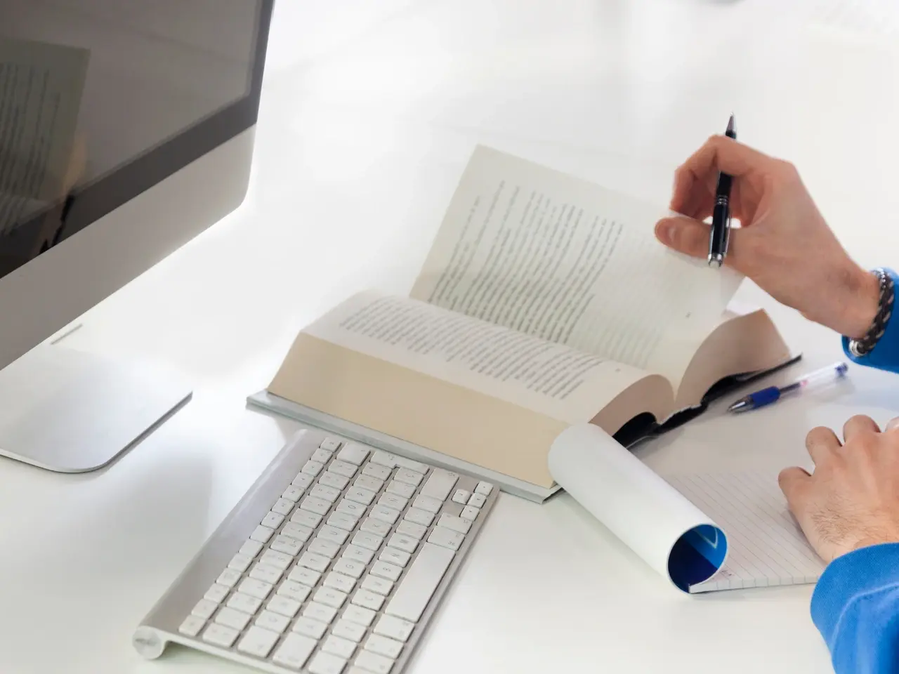 Person taking notes at a desk with a computer and open book, representing document translation.