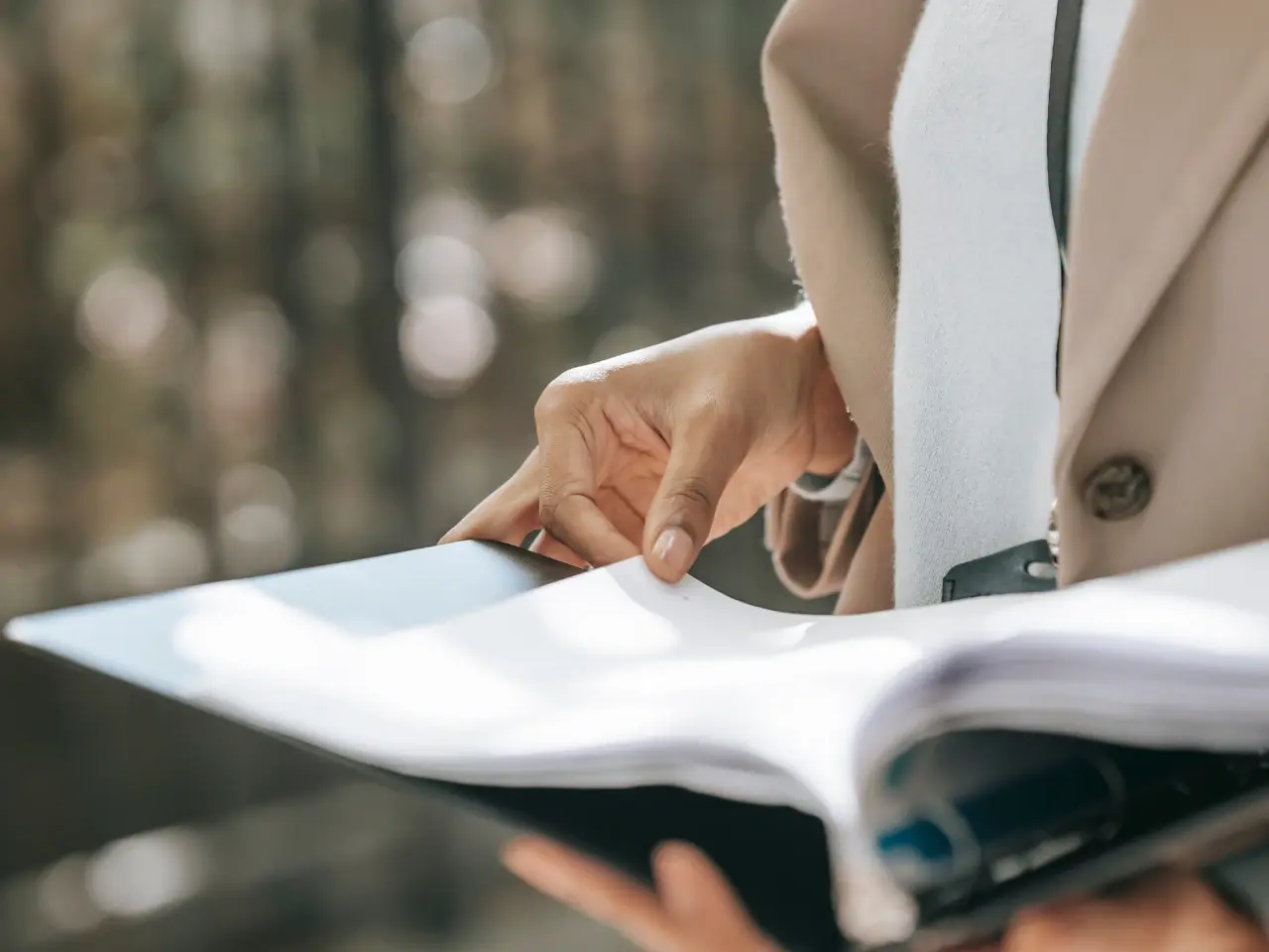 A close-up of a person in a beige coat flipping through a folder with documents, suggesting a review of official paperwork or translated certificates.