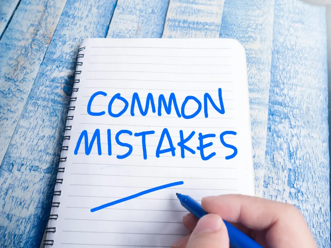 A spiral notebook on a blue wooden surface with the words “COMMON MISTAKES” written in bold blue marker, and a hand holding the marker underlining the phrase.