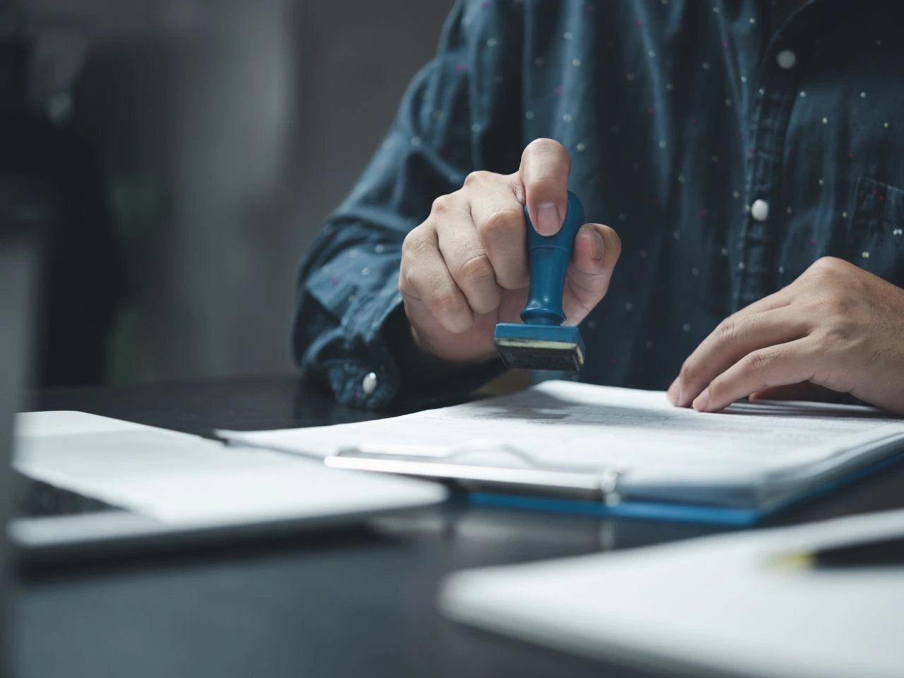 Person using a blue stamp to certify a stack of official documents, representing the validation process in certified translation services.