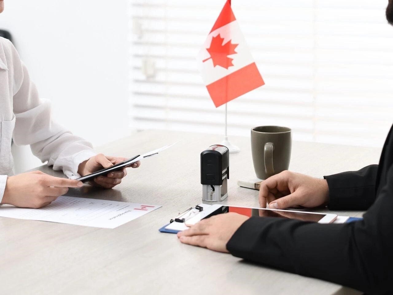 Two people reviewing Canadian immigration documents at a desk with a tablet, stamp, and Canadian flag, representing certified translation services for IRCC applications.