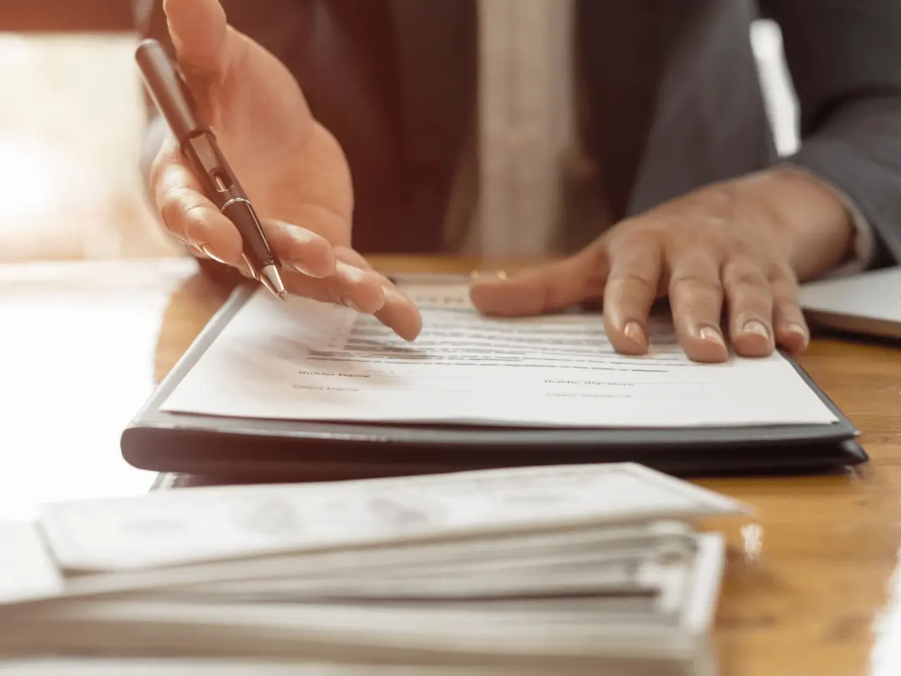 Person reviewing or signing official documents with a pen — close-up of hands at a desk.