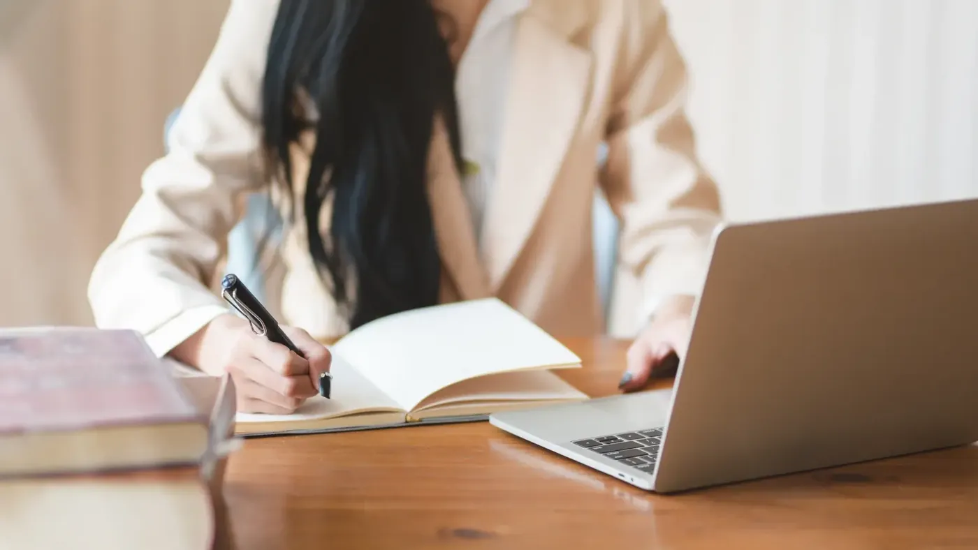 Woman taking notes while working on a laptop, representing the process of preparing and reviewing official document translations.