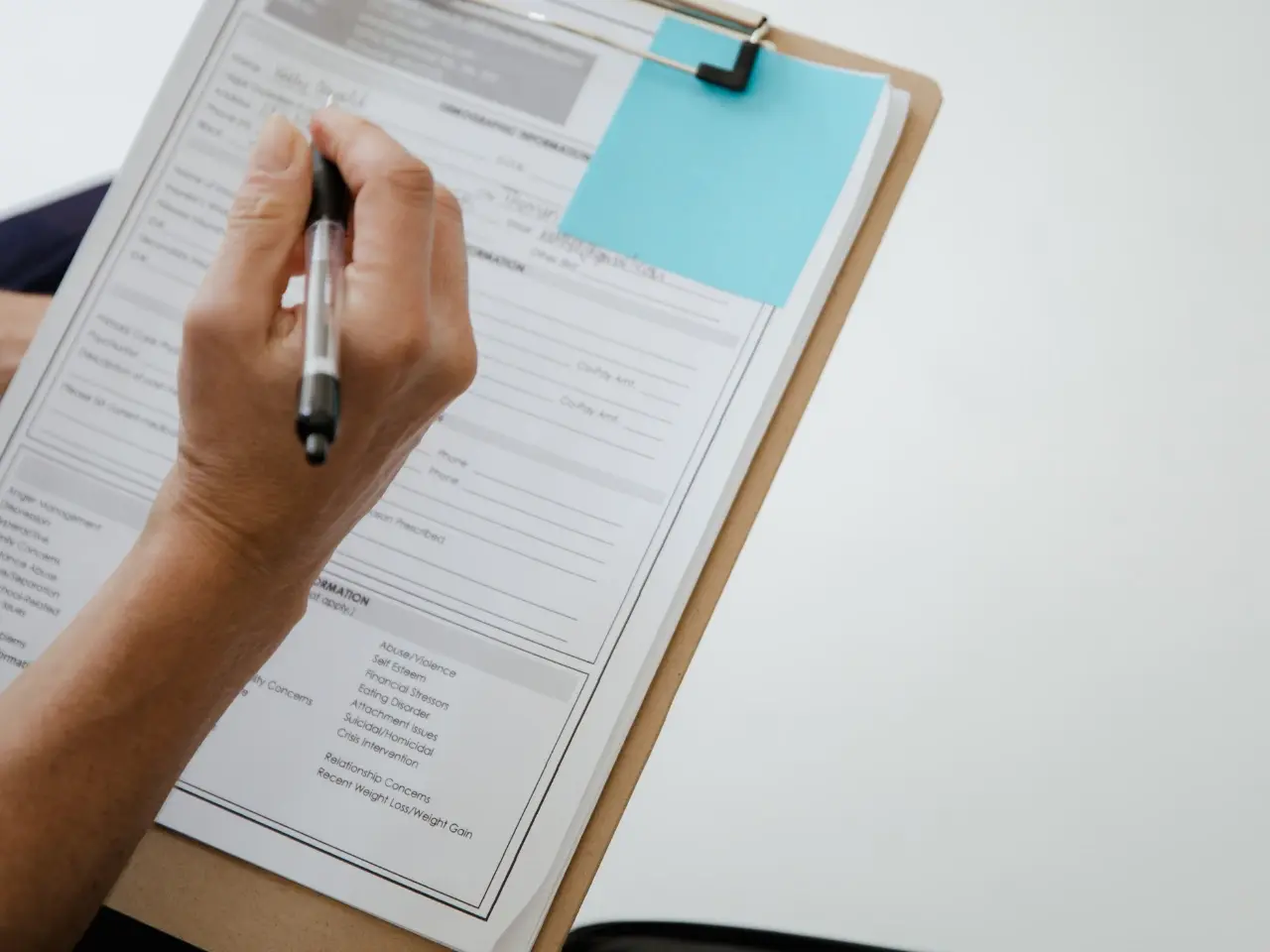 Person completing a birth certificate application form on a clipboard.