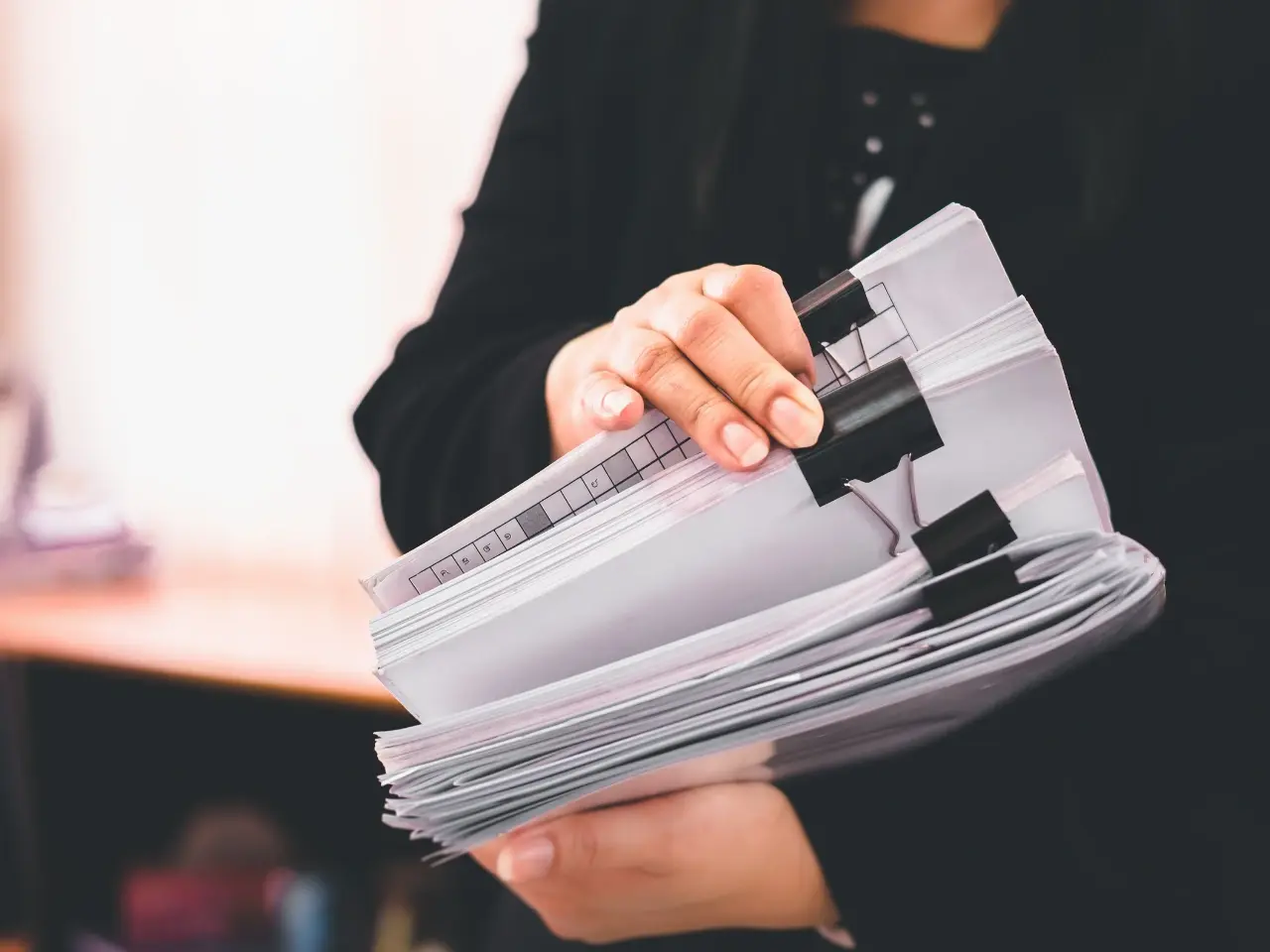 Close-up of a person holding multiple clipped document files, symbolizing the preparation of paperwork for legalization in Canada.