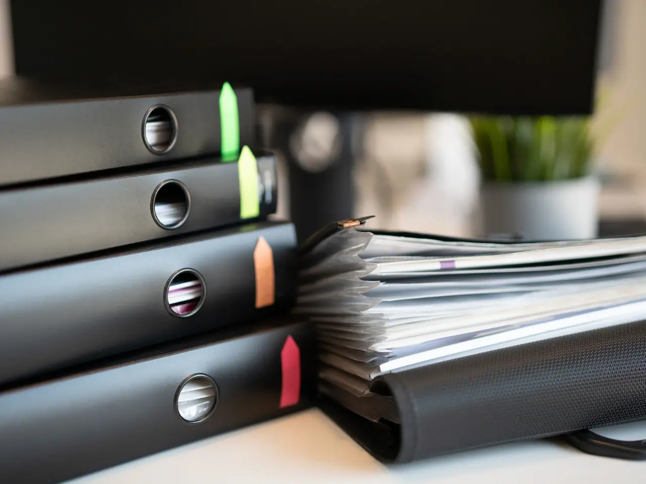 Stack of black binders and a filled accordion folder on a desk, representing organized storage of translated and certified documents.