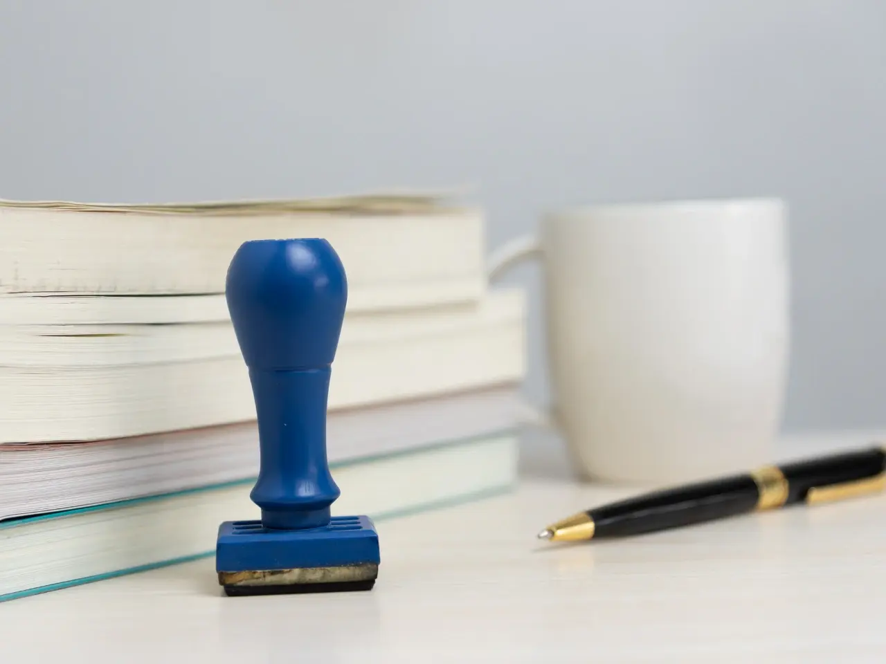 Blue certification stamp placed beside stacked books, a pen, and a white mug, symbolizing official approval of translated documents.