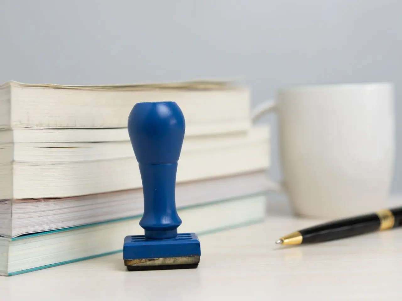 Blue certification stamp placed in front of stacked books, with a pen and coffee mug nearby, symbolizing the official approval process in certified translation work.