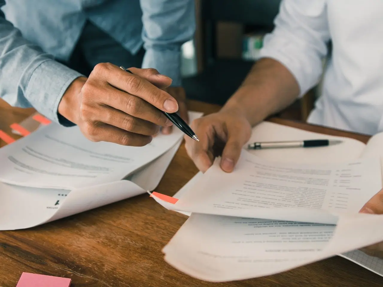 Two people reviewing and discussing official documents with notes and tabs, representing the collaborative review process in certified translation services.