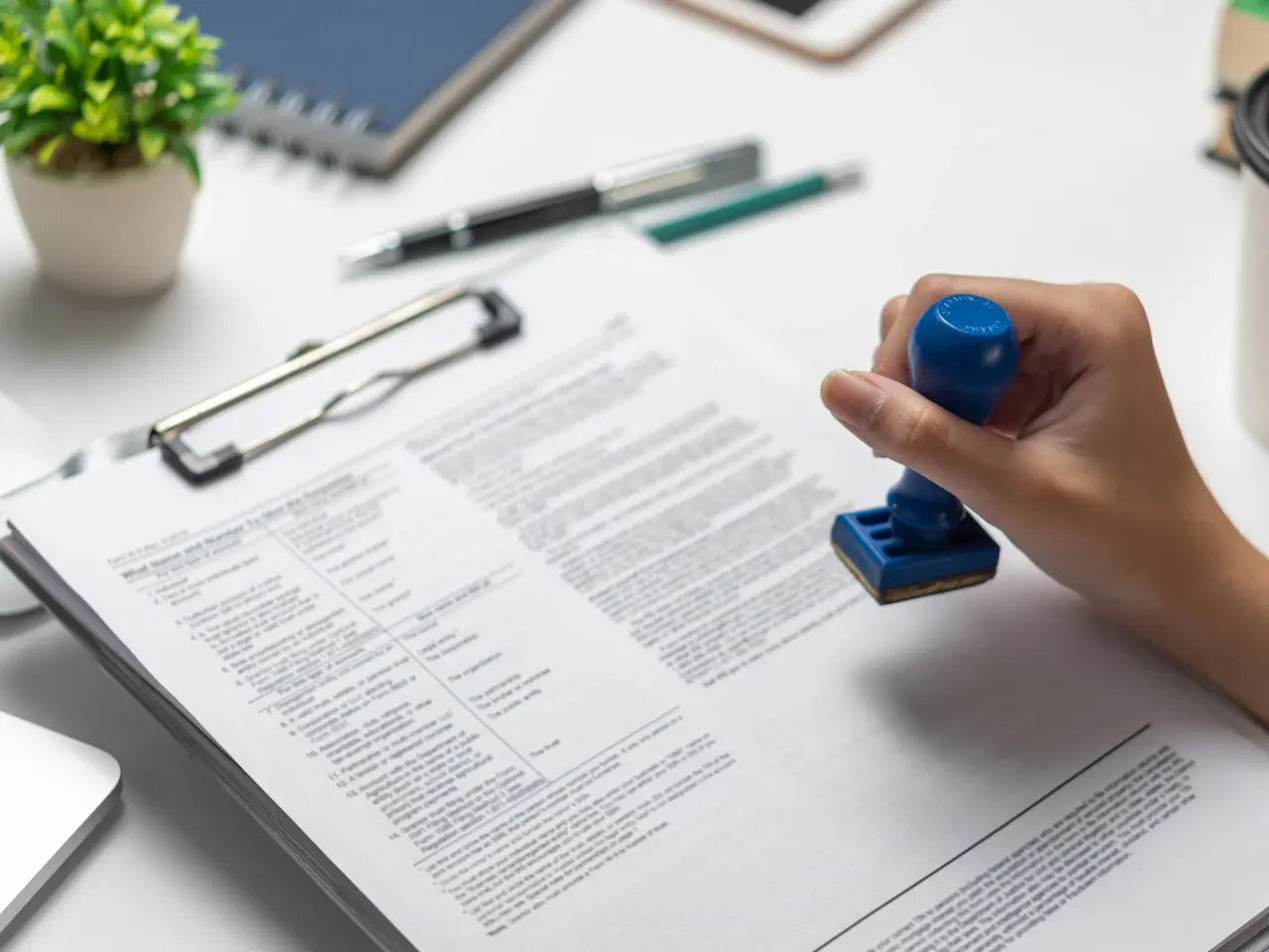 Hand holding a blue stamp over a legal document on a clipboard, indicating certification or official approval.