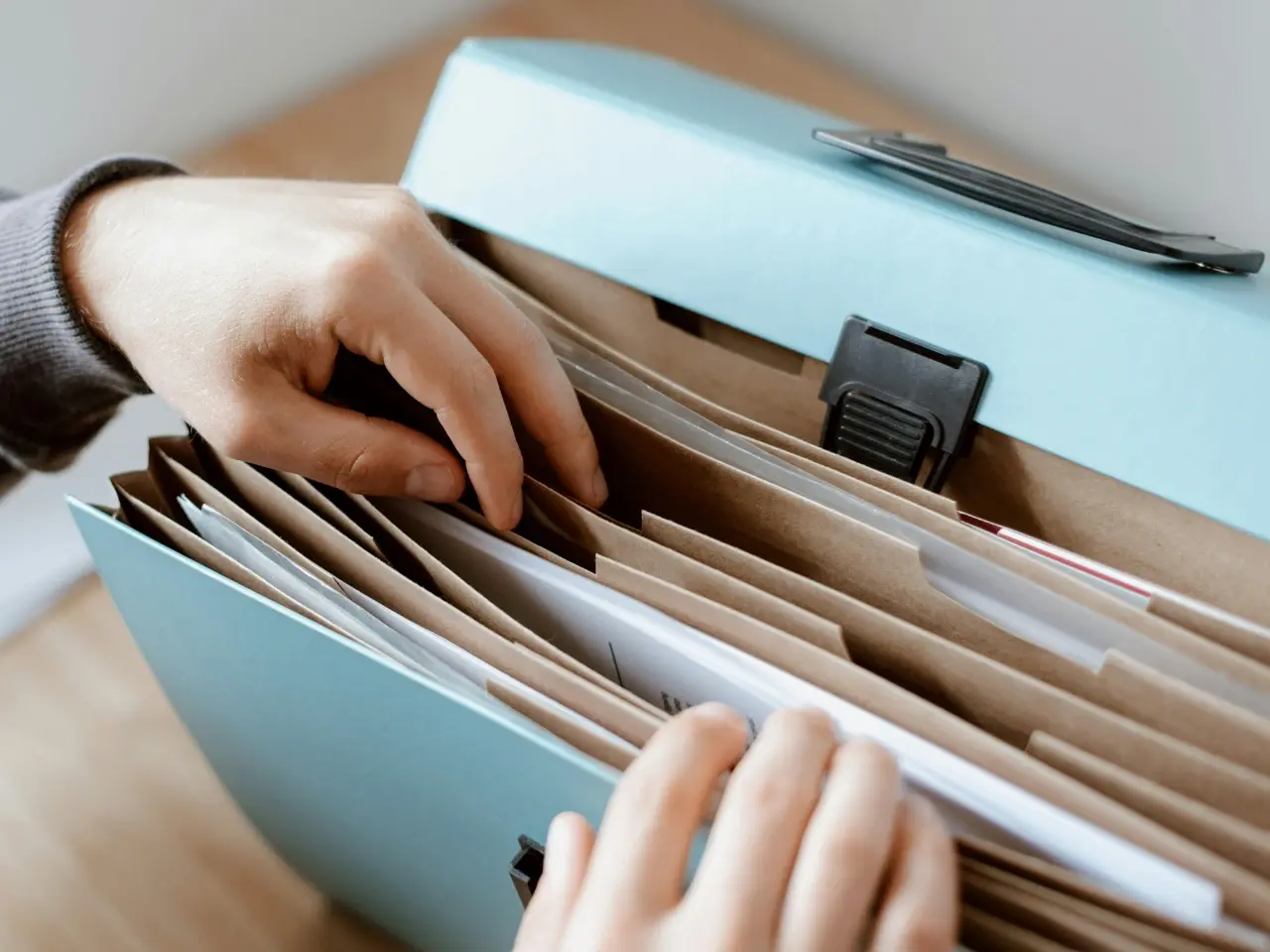Hands sorting through documents in a blue accordion file folder, organizing official paperwork.