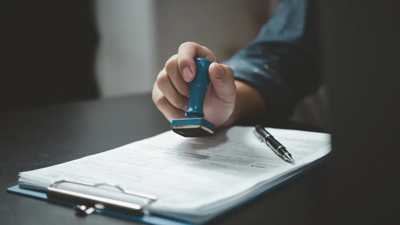 Close-up of a hand stamping a document on a clipboard, symbolizing notarization, legalization, or certified document translation.