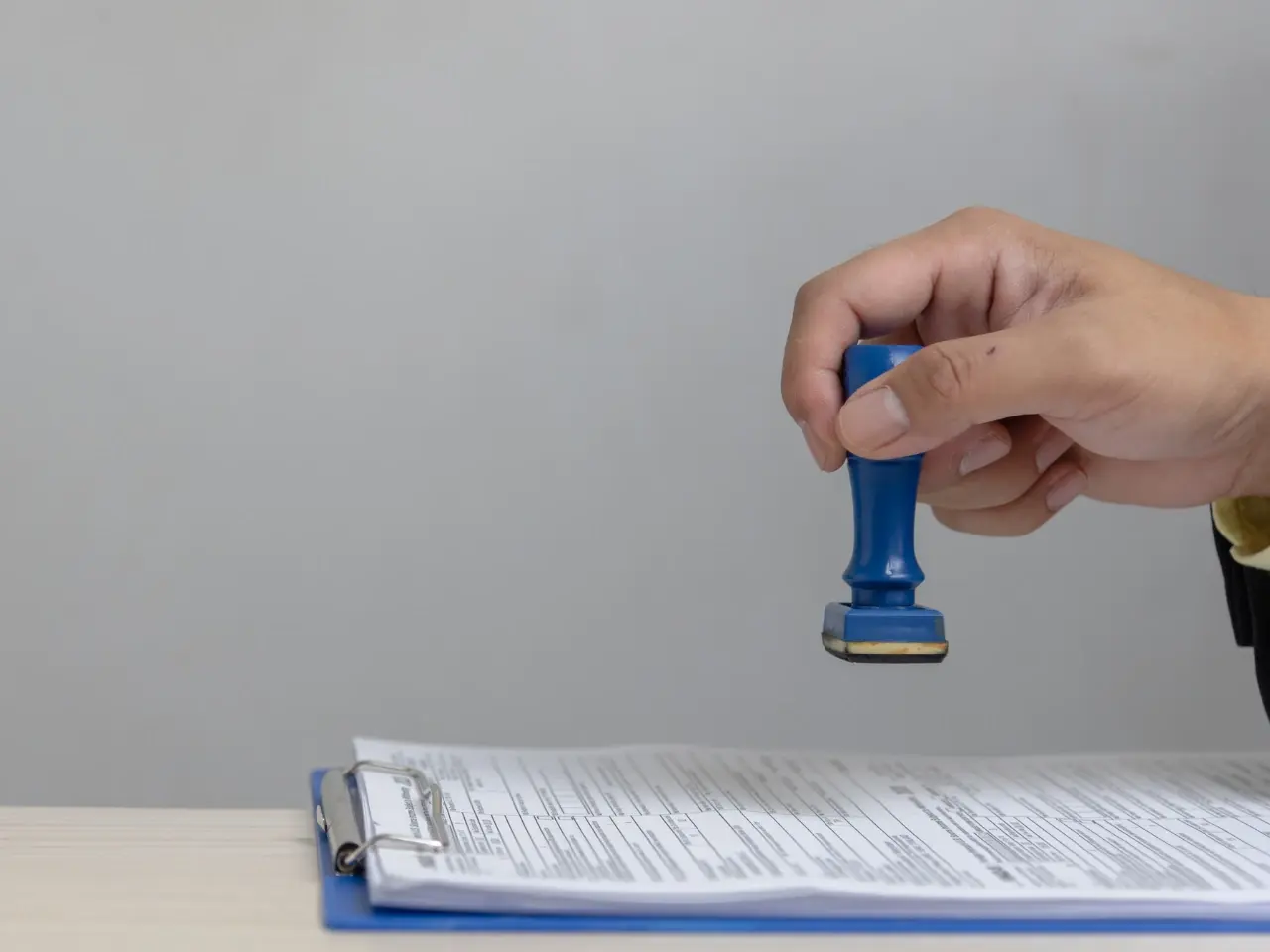Hand pressing a blue stamp onto a document on a clipboard, representing notarization, legalization, or certified document services.