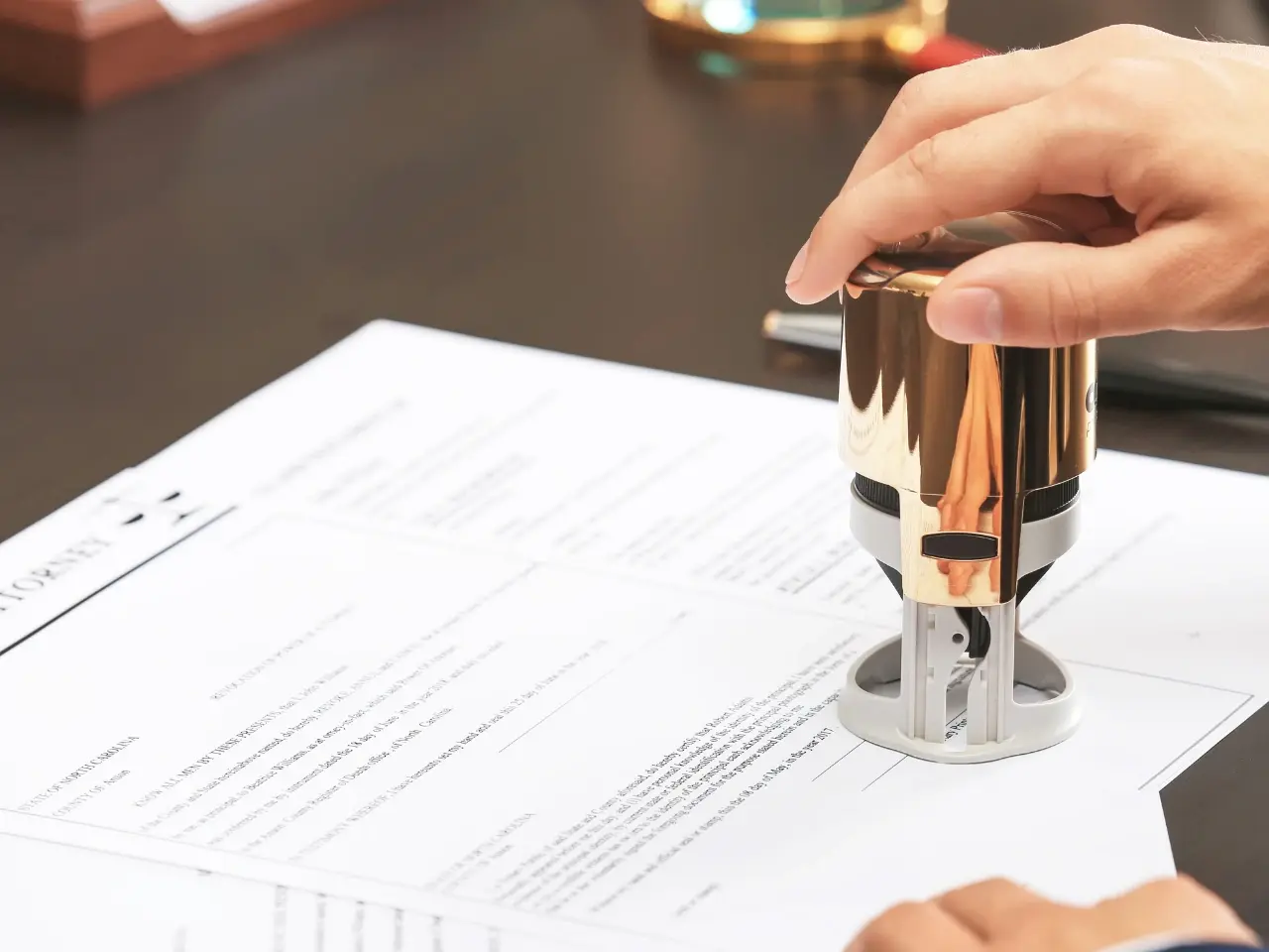 Close-up of a hand using a golden notary stamp on official documents, representing notarization, legalization, or certified document services.
