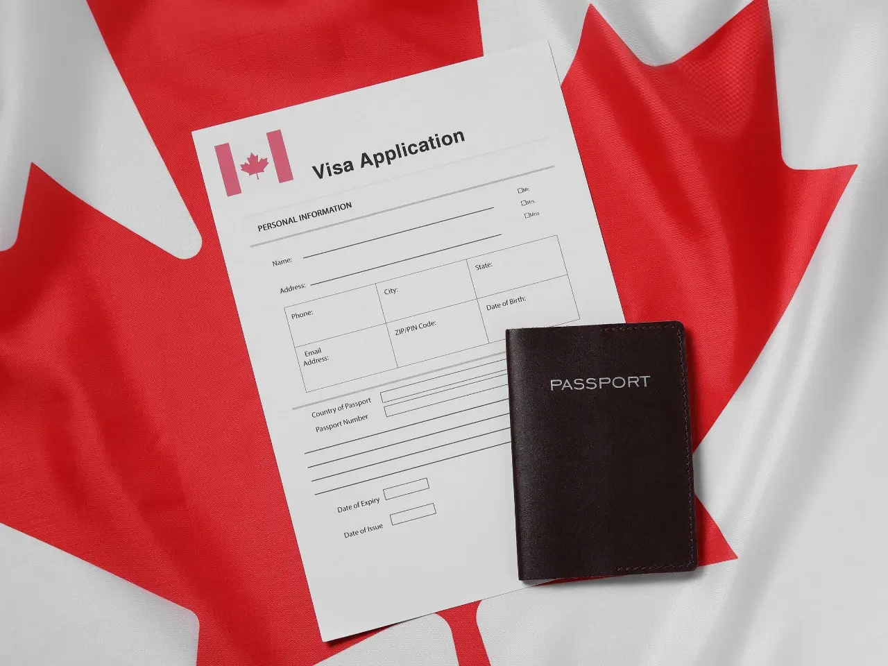 Canadian visa application form and passport placed on a Canadian flag, symbolizing immigration, visa processing, and official document preparation.