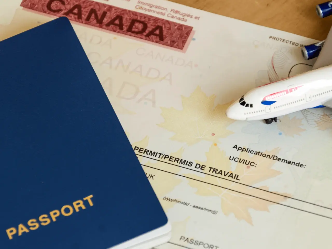 Passport placed on top of immigration documents with a toy airplane, symbolizing travel and official certification processes in Canada.