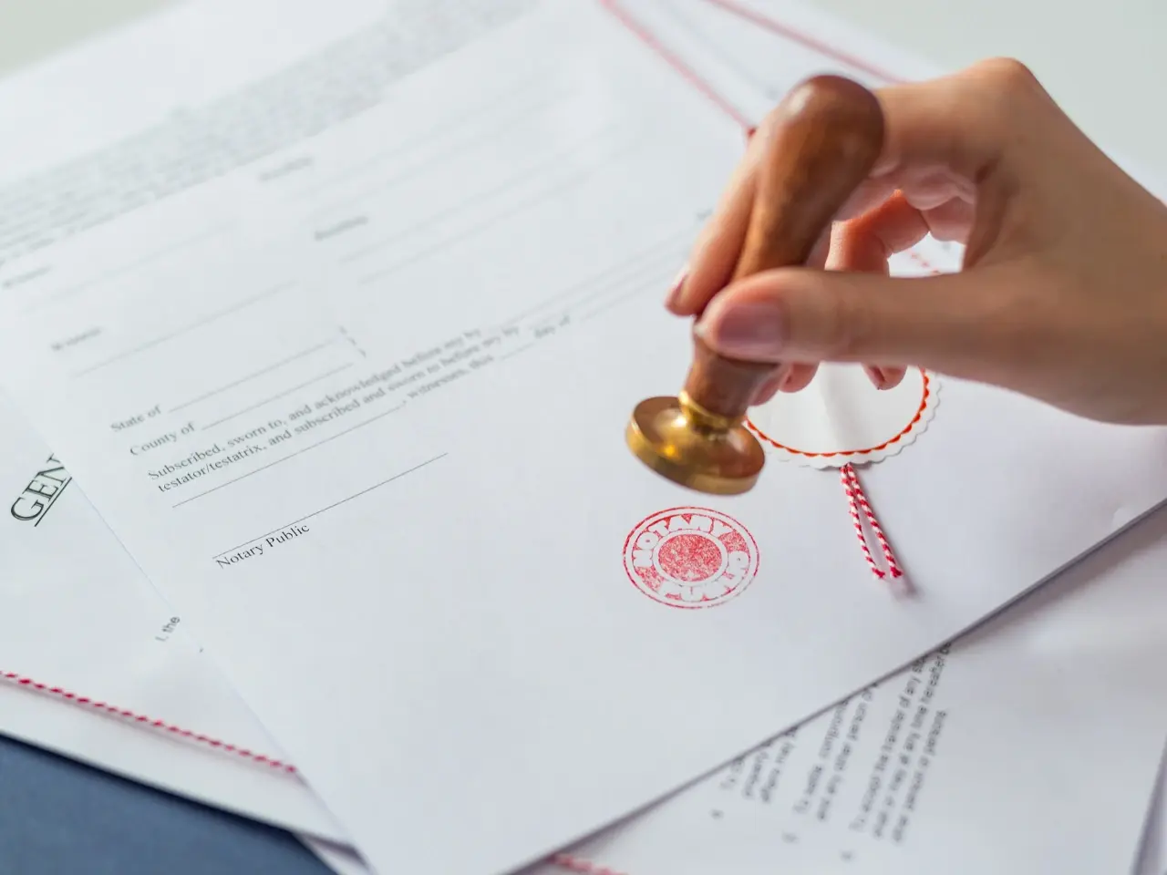 Two professionals reviewing and exchanging official documents across a desk, with a stack of paperwork and a clipboard labelled “Terms and Conditions” — representing a legal or contractual review process.