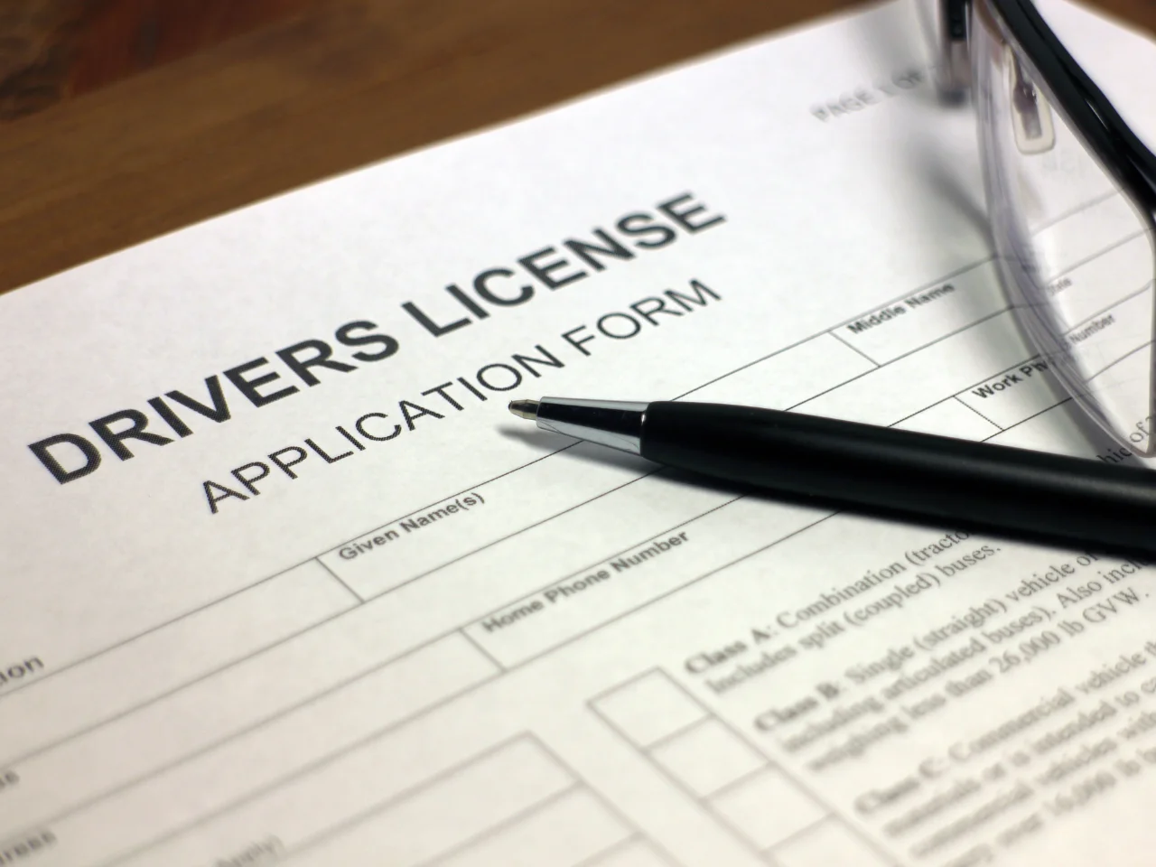 Driver's licence application form with a pen and eyeglasses, representing the Quebec driver's licence application and SAAQ exchange process.