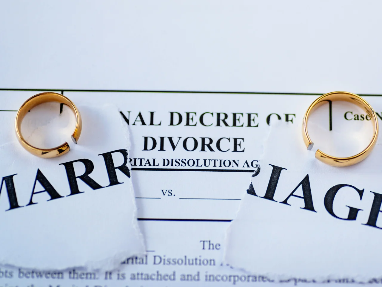 Torn marriage certificate and final decree of divorce with wedding rings representing the legal end of a marriage.
