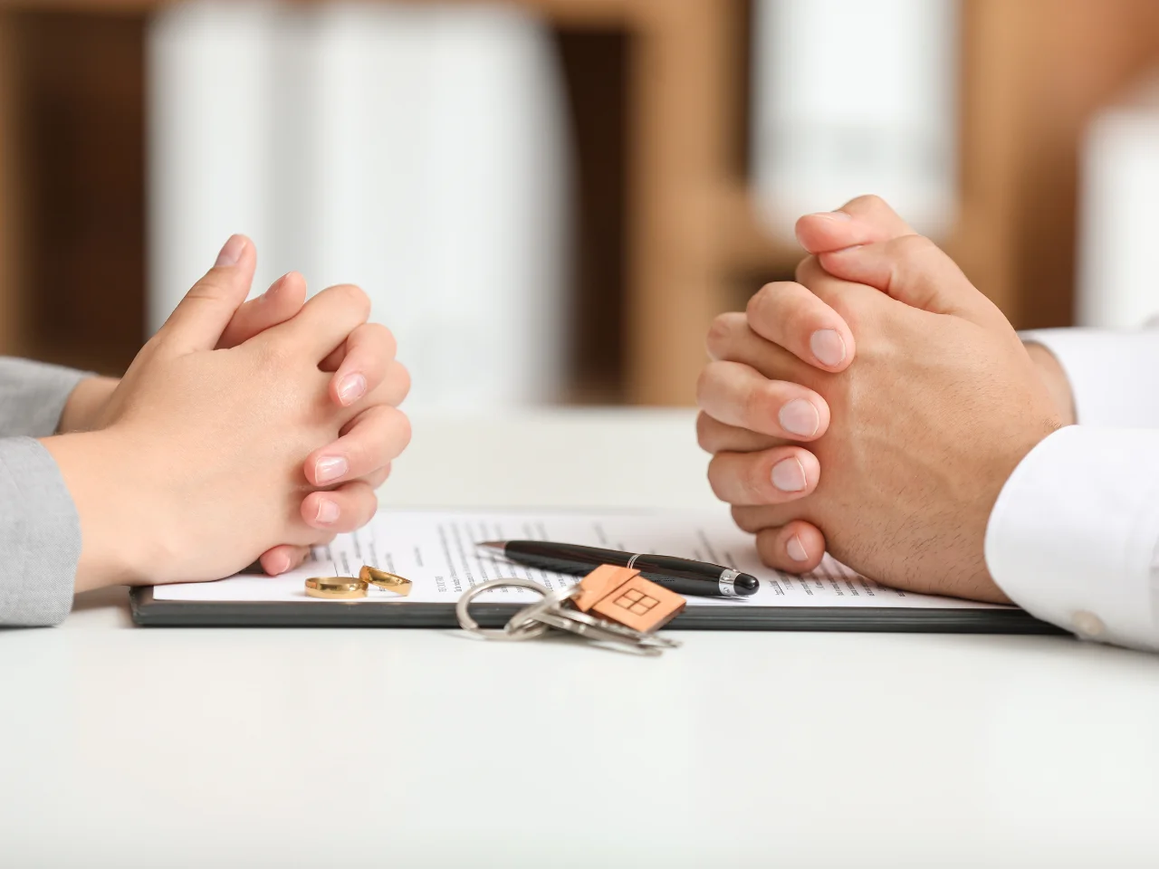 Couple discussing divorce documents with wedding rings and house keys on the table during a legal consultation.