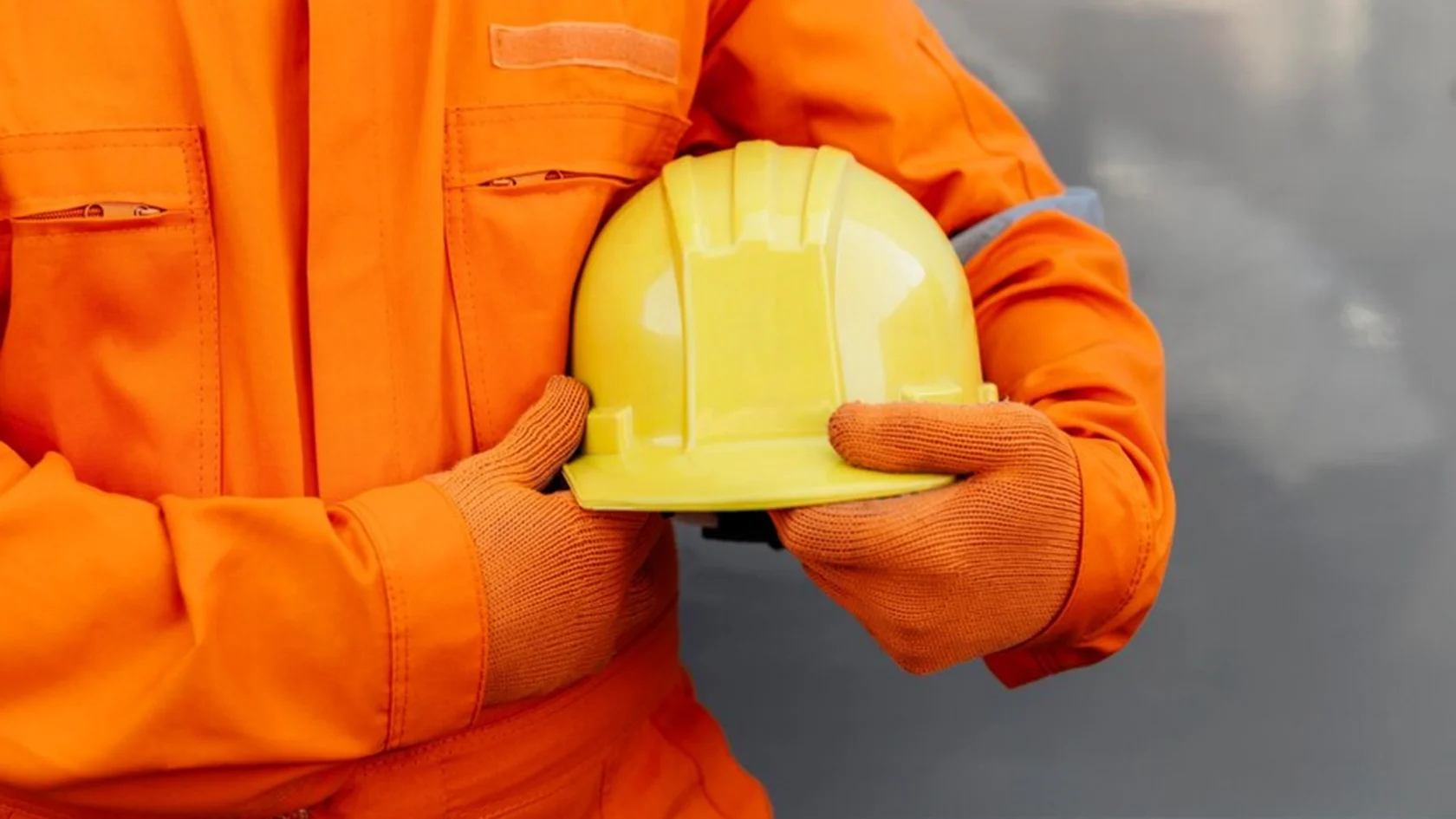 Engineer in safety gear holding a yellow hard hat at a construction site.