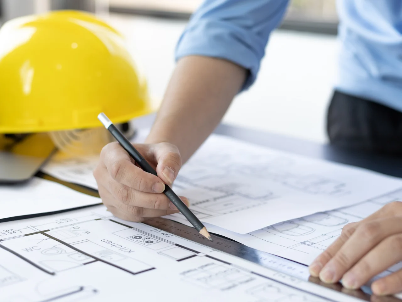 Engineer reviewing architectural plans with a pencil and ruler beside a hard hat.