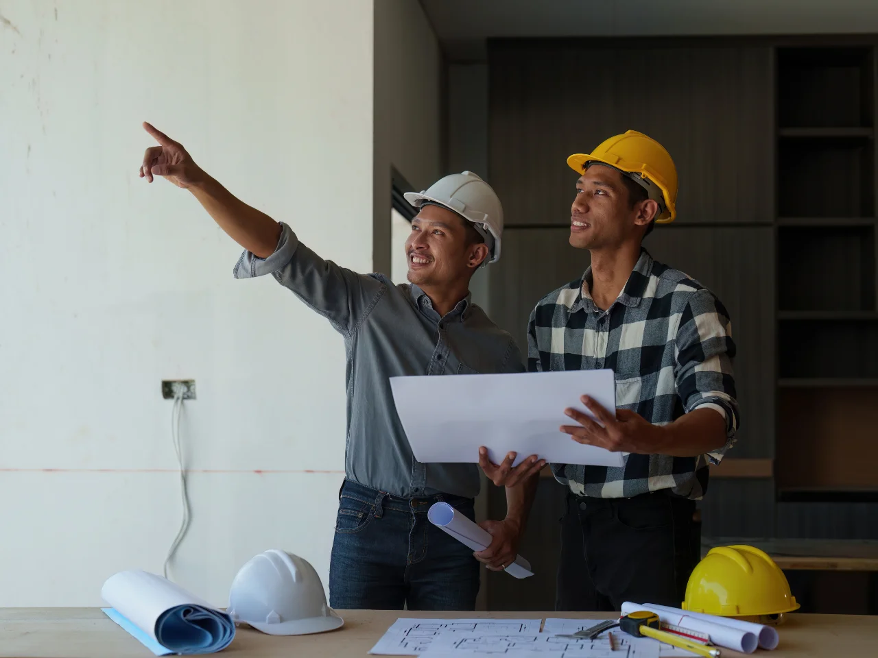 Two engineers in hard hats discussing building plans at a construction site.